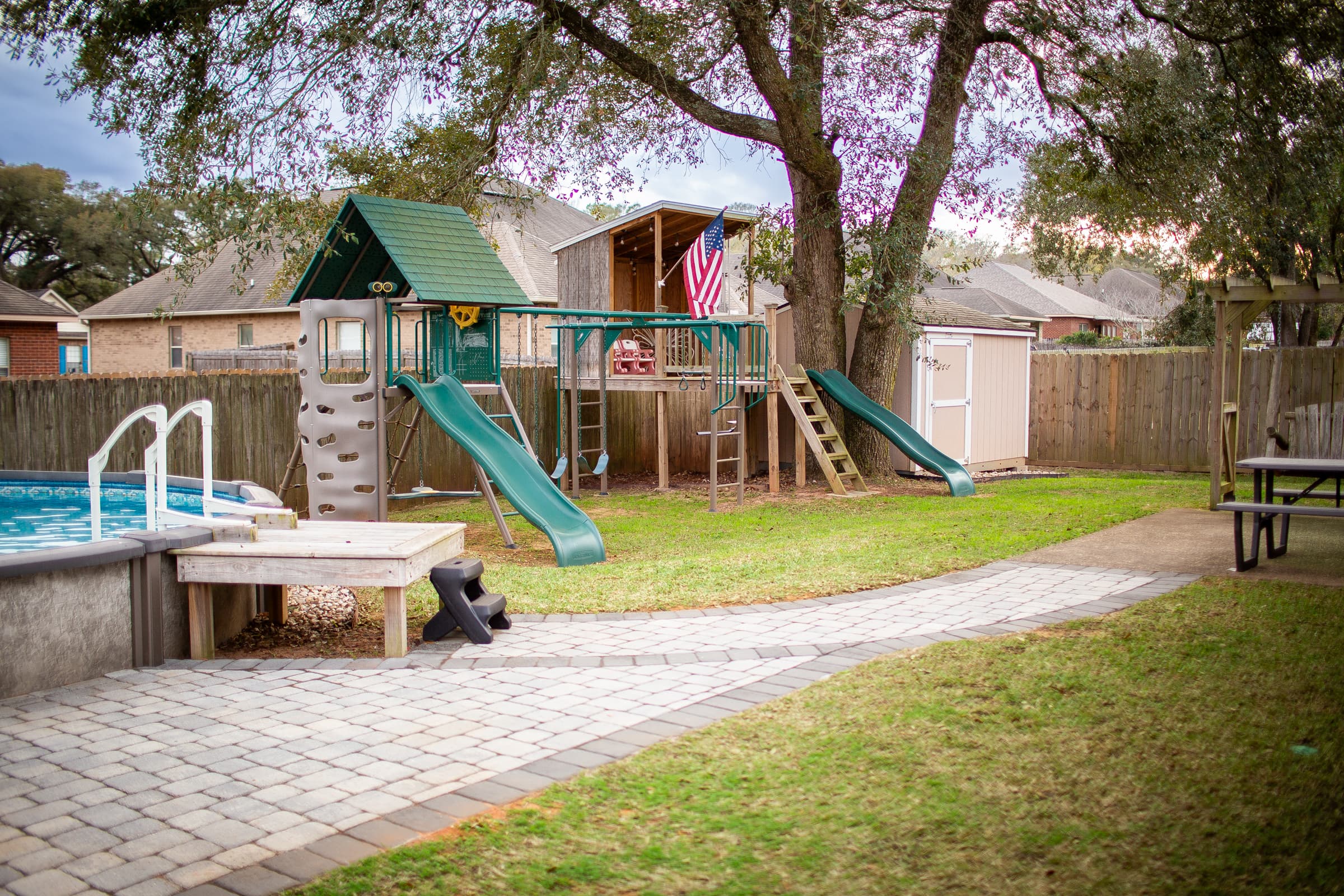 Backyard with playset, pool, and paver path